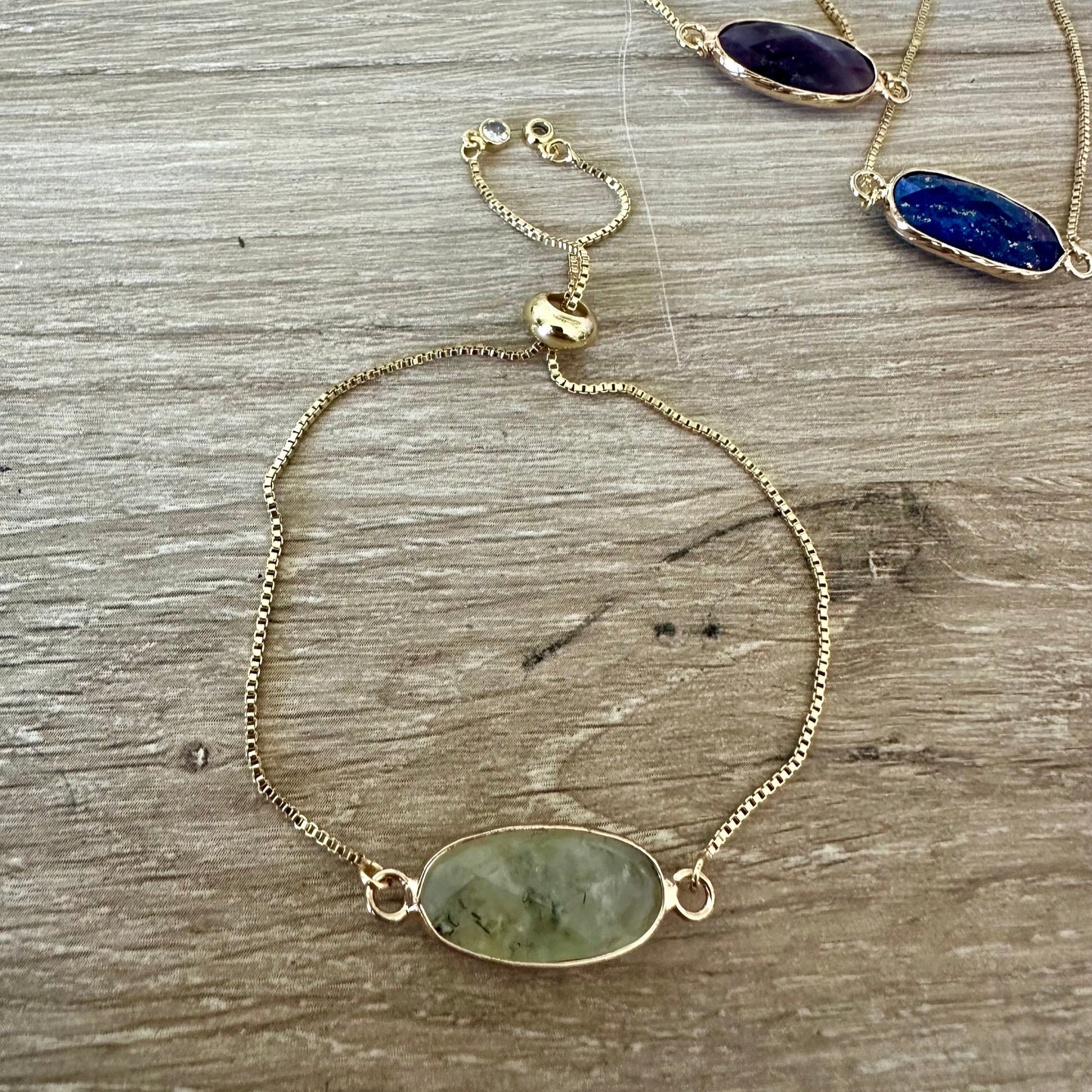 Gold bracelet with gemstone pendants on a wooden surface