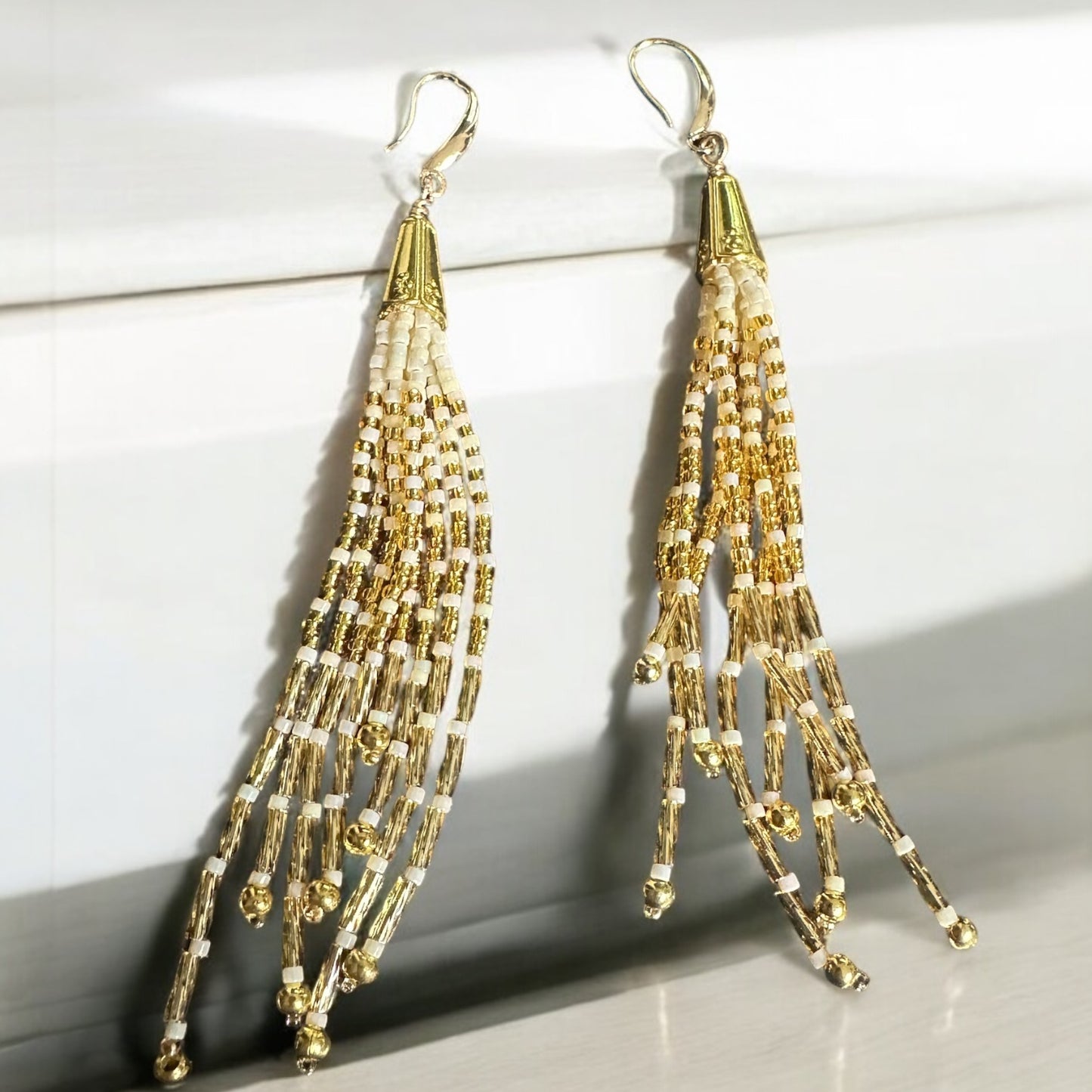 Tassel earrings with gold filled ear hook in gold and cream colors. On contertop