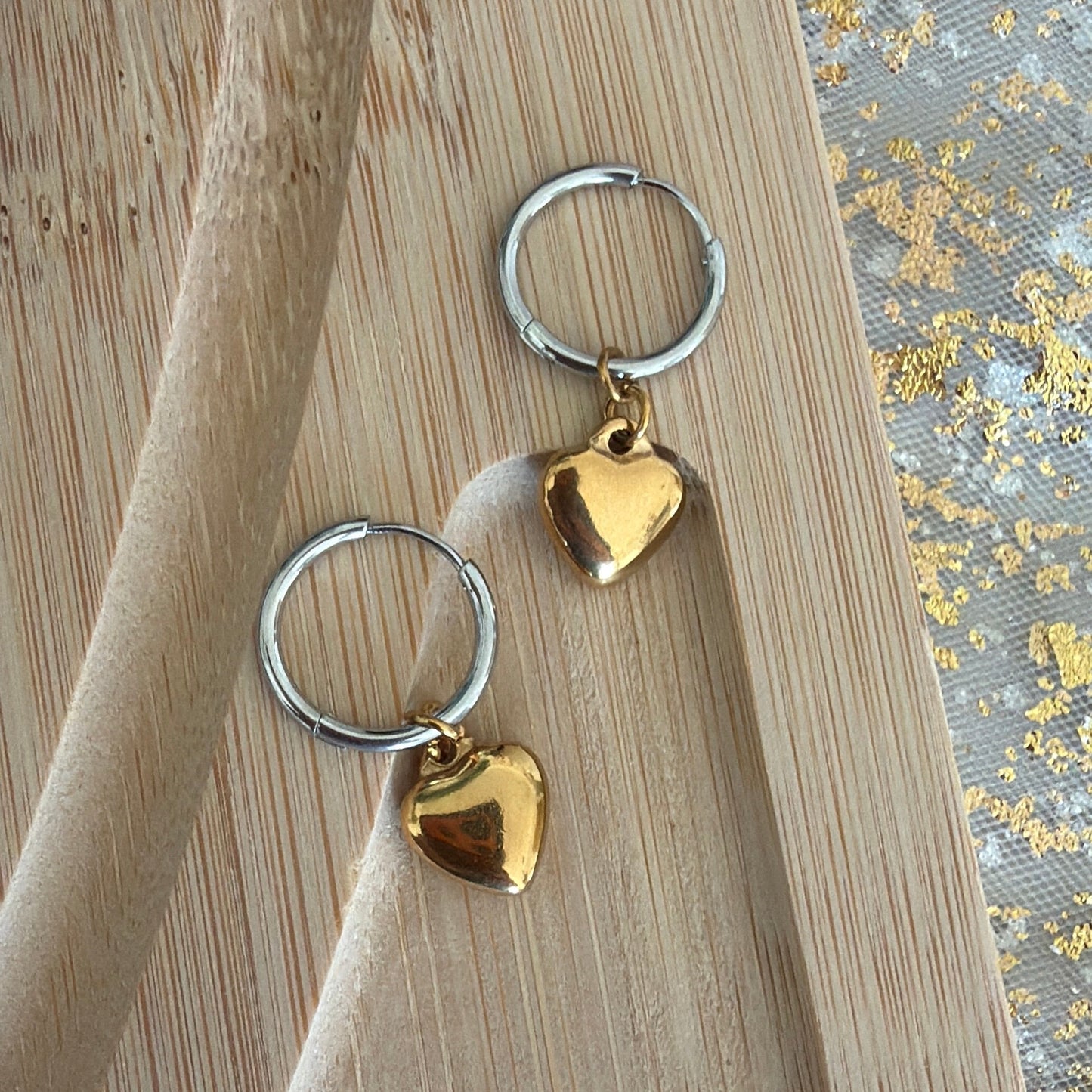 Mixed tone hoop earrings with heart shapes on a wooden surface.