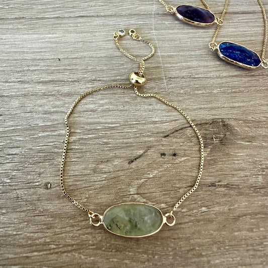 Gold bracelet with gemstone pendants on a wooden surface