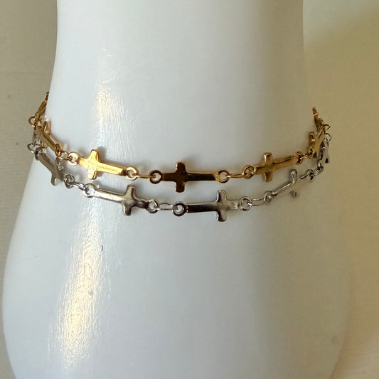 Gold and silver cross bracelet on a mannequin wrist against a neutral background