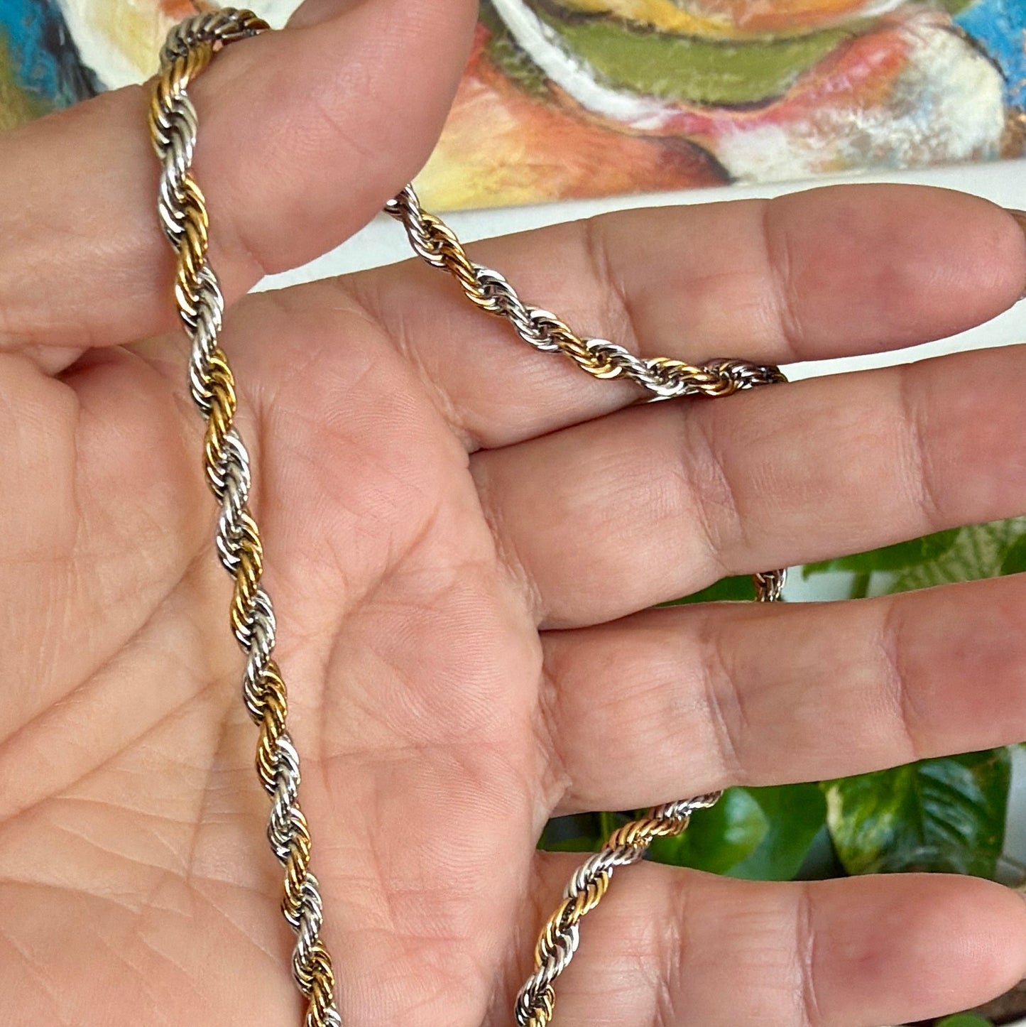 Gold and silver chain held in a hand with a colorful background