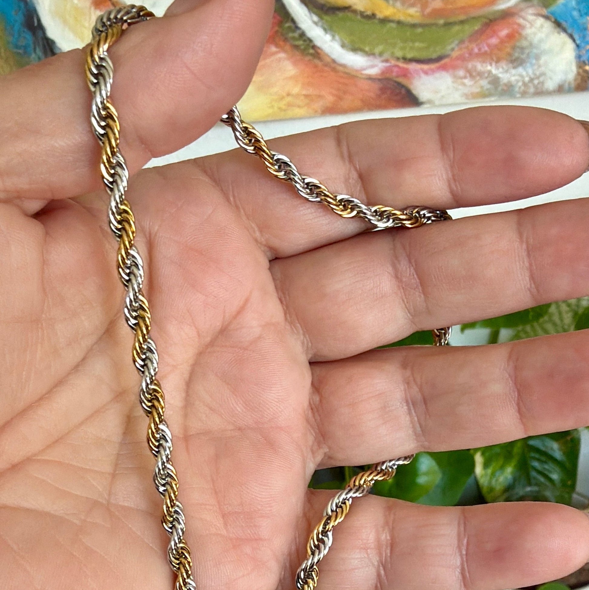 Gold and silver chain held in a hand with a colorful background