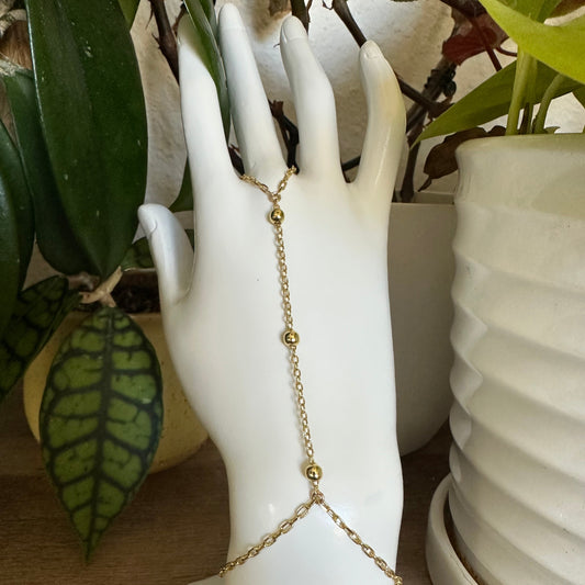 gold hand chain bracelet on hand mannequin with green plants in background