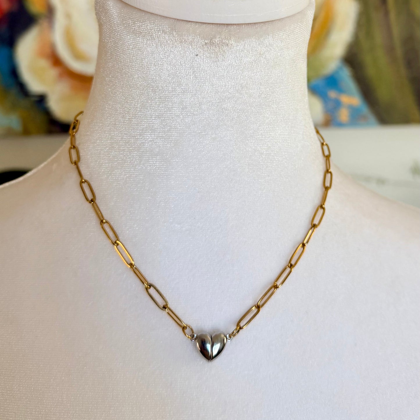 Gold chain necklace with a heart pendant on a mannequin bust against a colorful floral background.