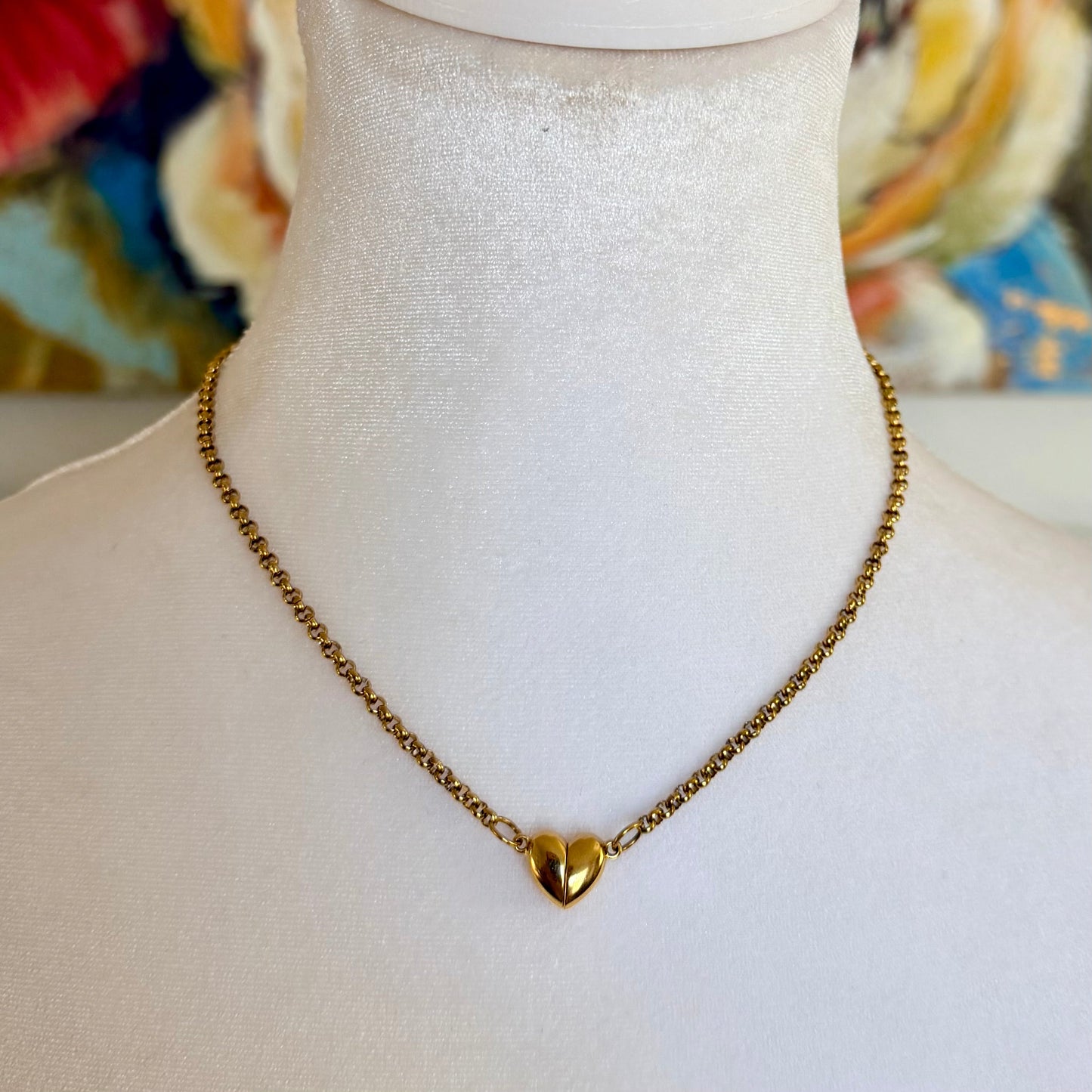 Gold necklace with a heart pendant on a mannequin against a colorful abstract background