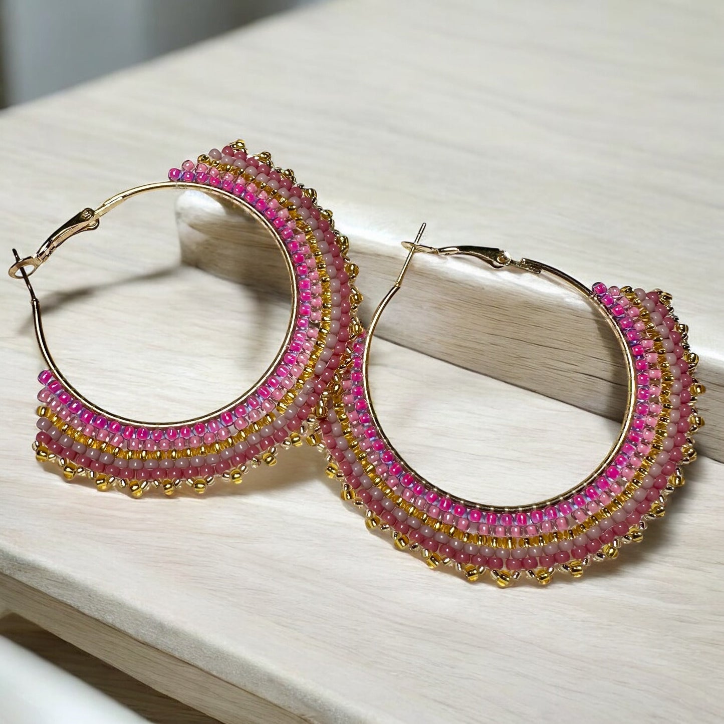 Beaded earrings adorned with rose and mauve toned seed beads on table