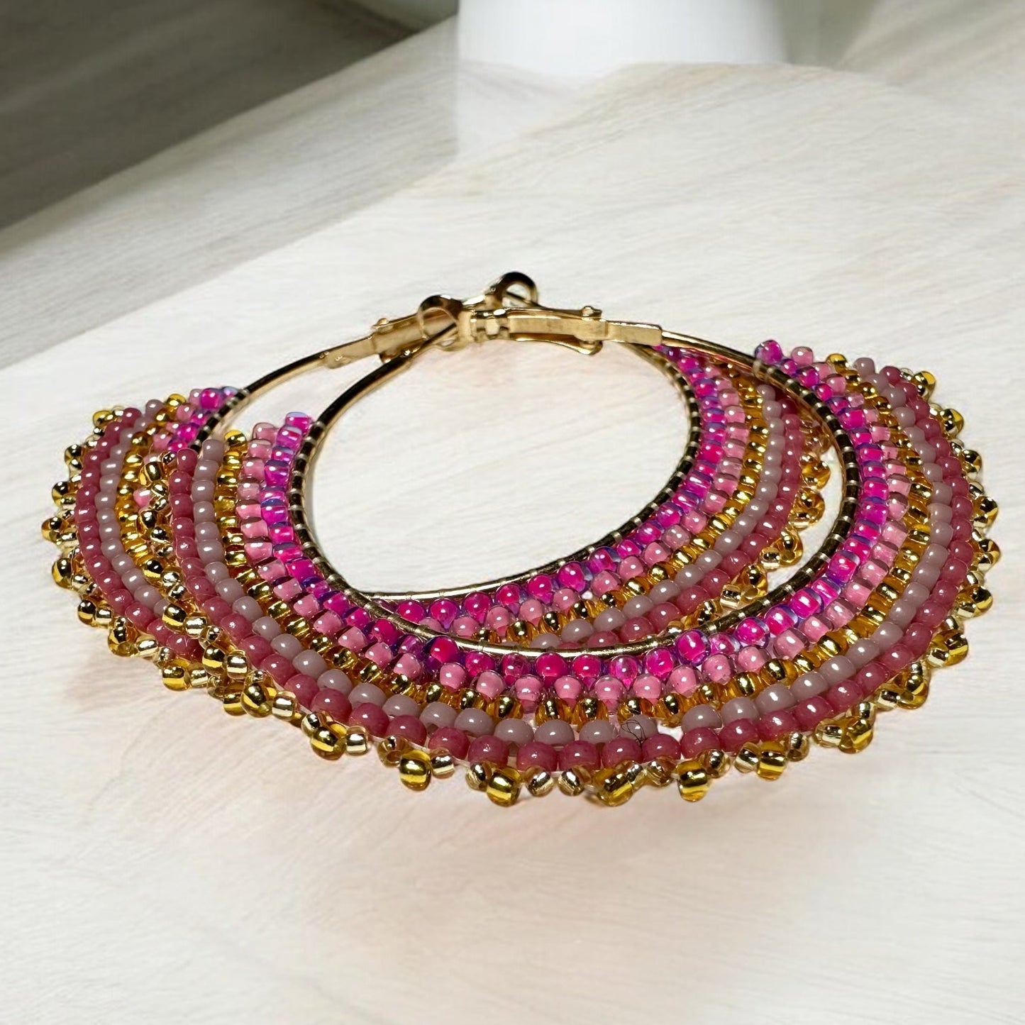 Beaded earrings adorned with rose and mauve toned seed beads on table