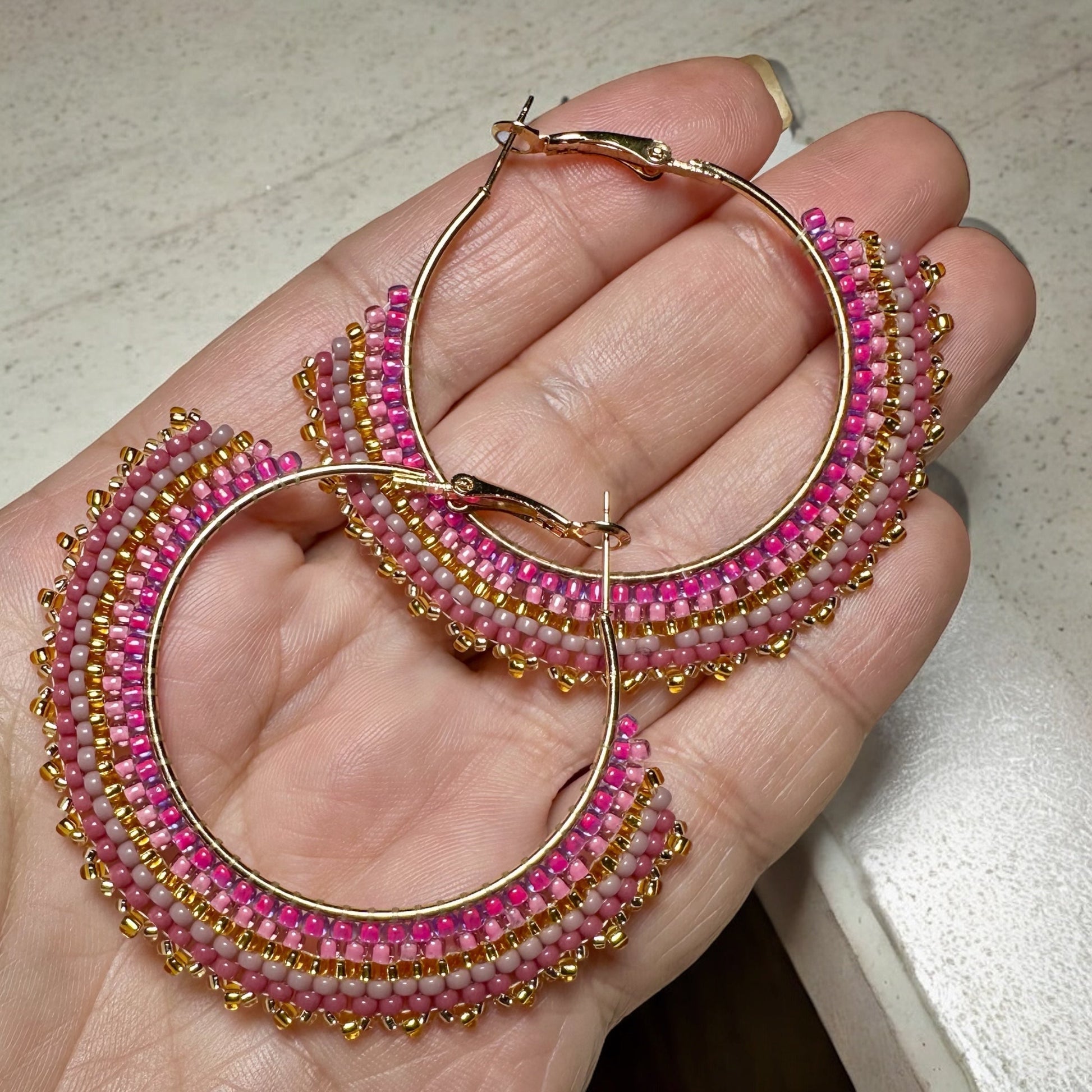 Beaded earrings adorned with rose and mauve toned seed beads handheld