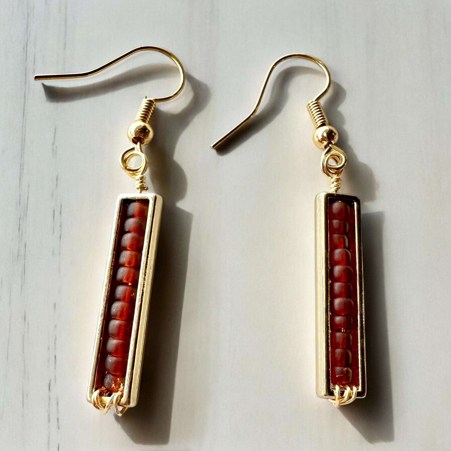 A pair of spectrum strips  beaded earrings earrings in gold and auburn on table