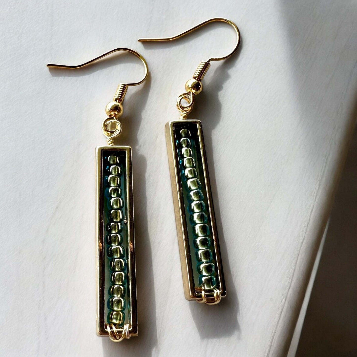 A pair of spectrum strips  beaded earrings earrings in green and gold on table