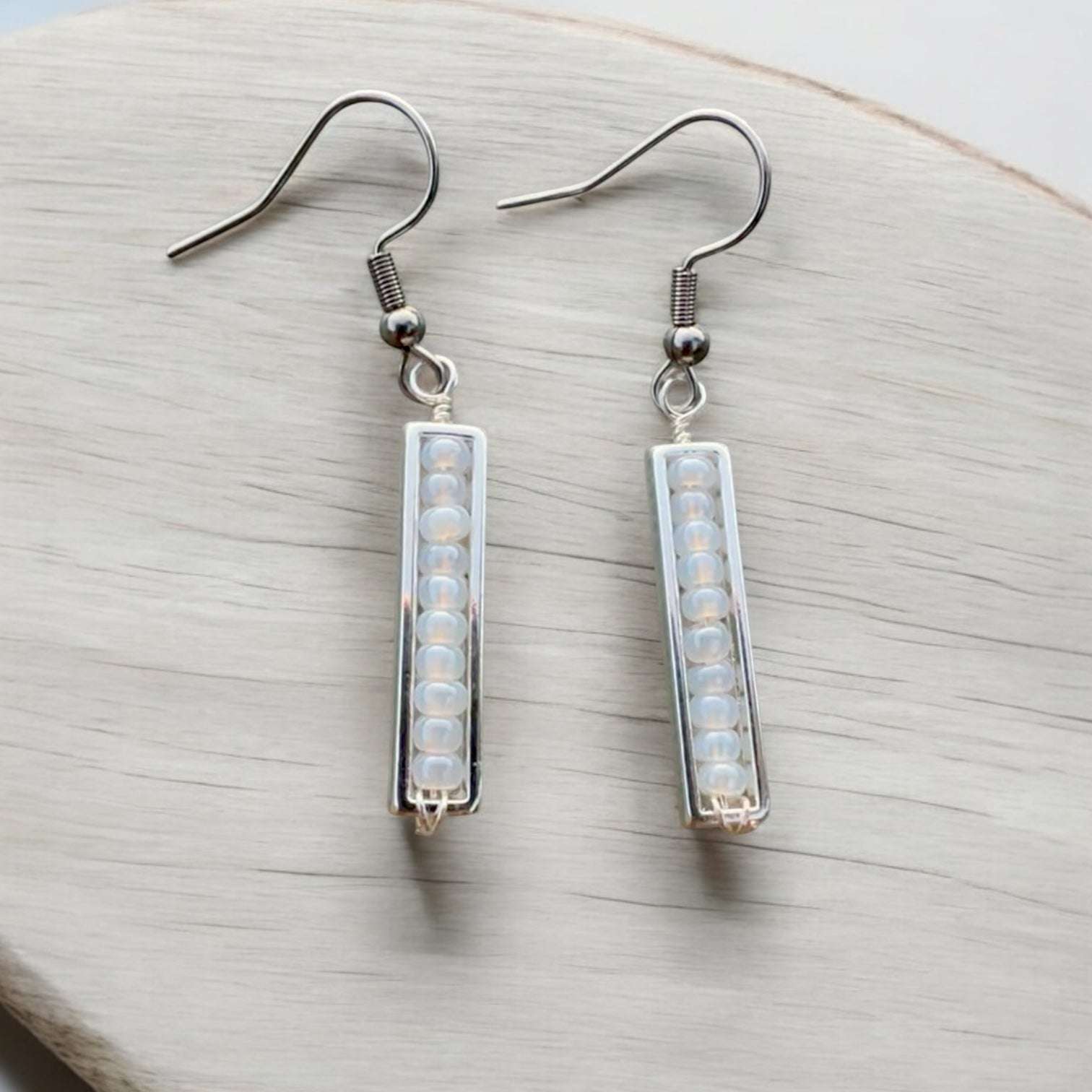 Spectrum strips earrings in stainless steel with white beads on a table.