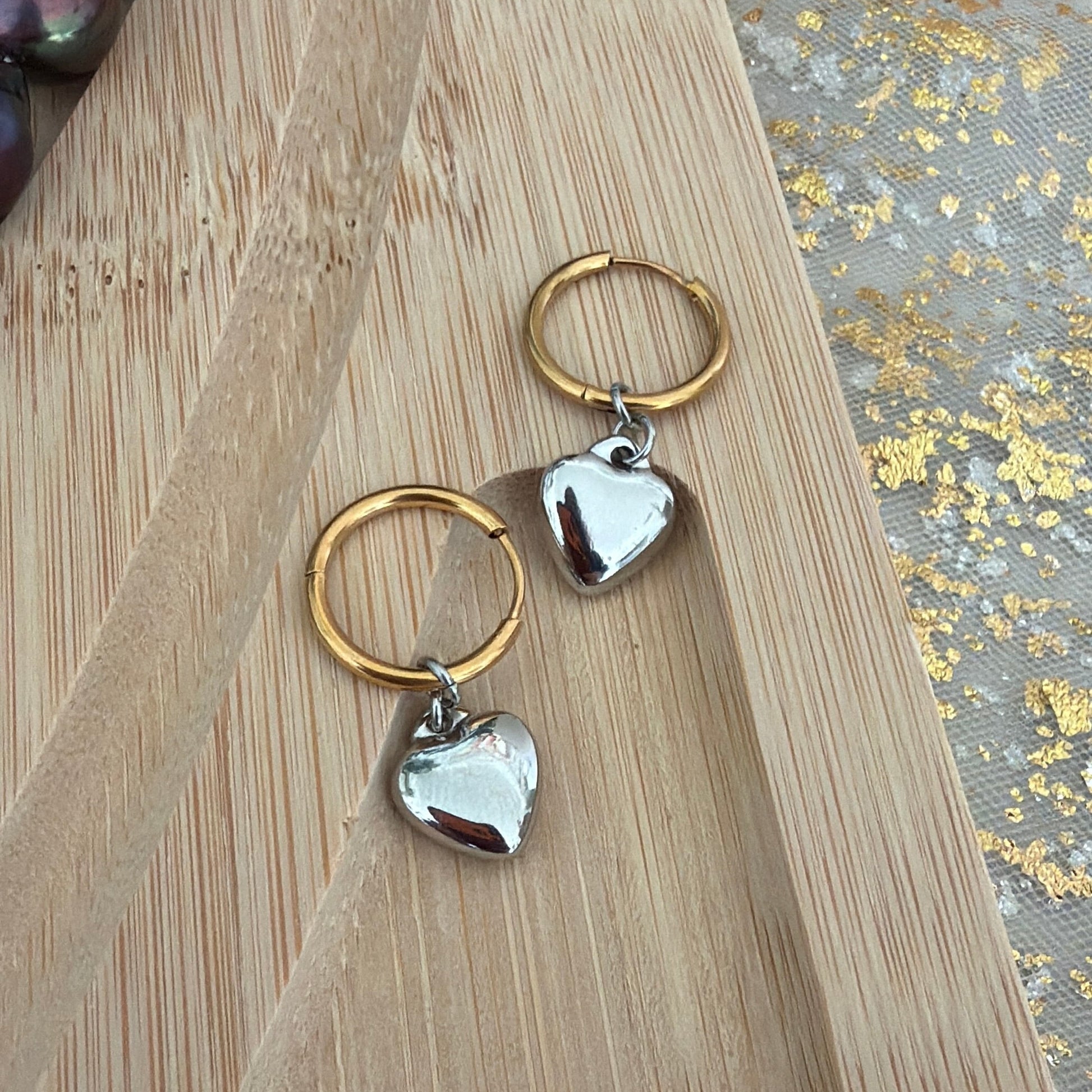 Mixed tone hoop earrings with heart shapes on a wooden surface.