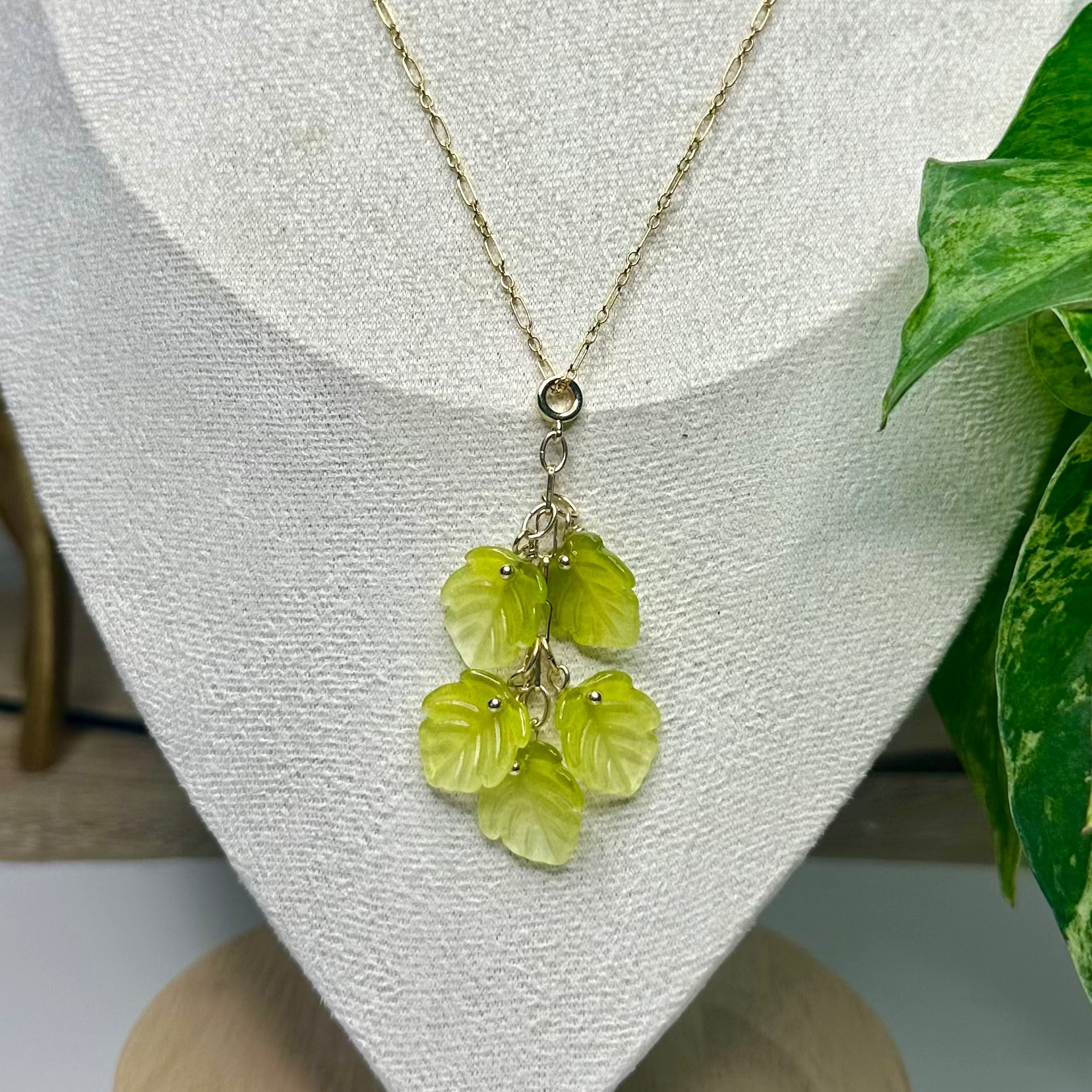 Necklace with green pendant on a mannequin bust, plant and decorative items in the background