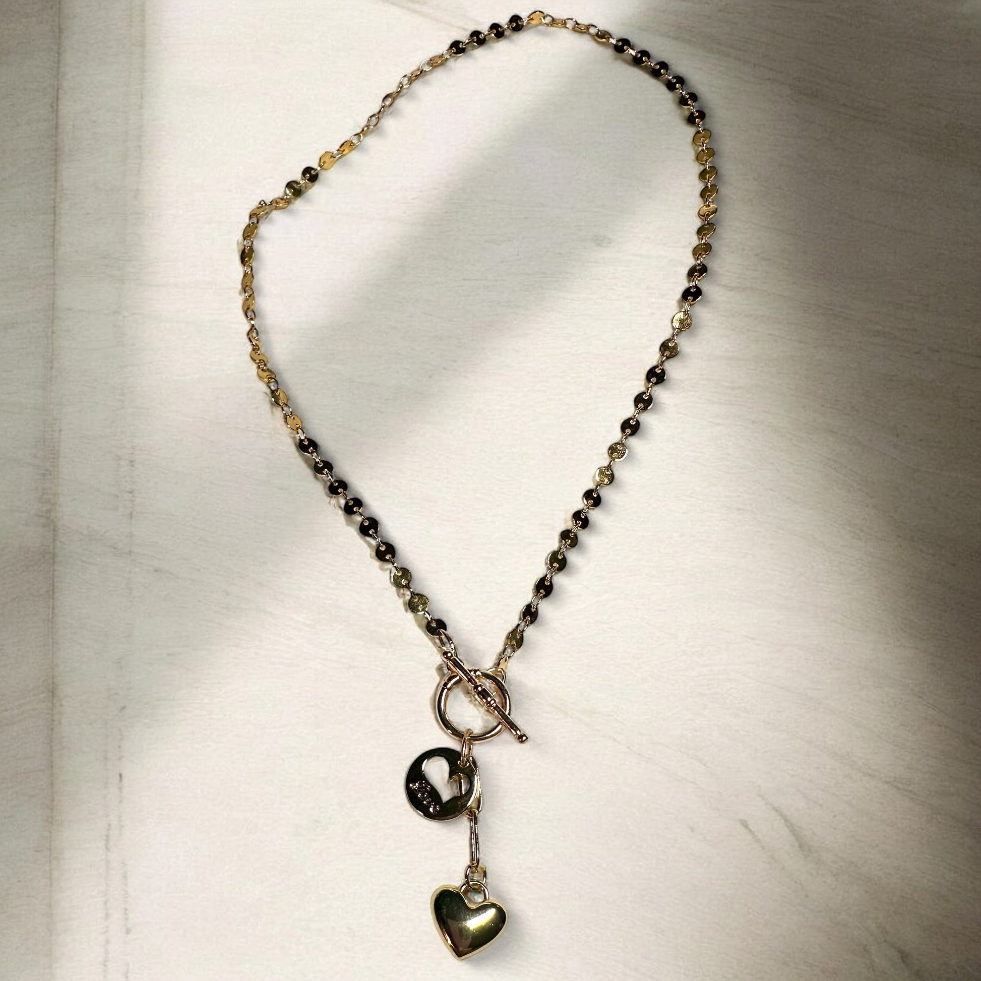 Gold-filled necklace with disc chain and  front closure toggle clasp with two heart pendants on table